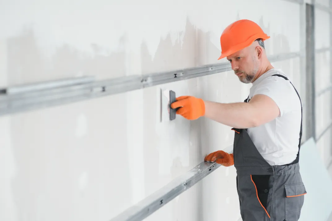 A man using a trowel for drywall plastering of the house.