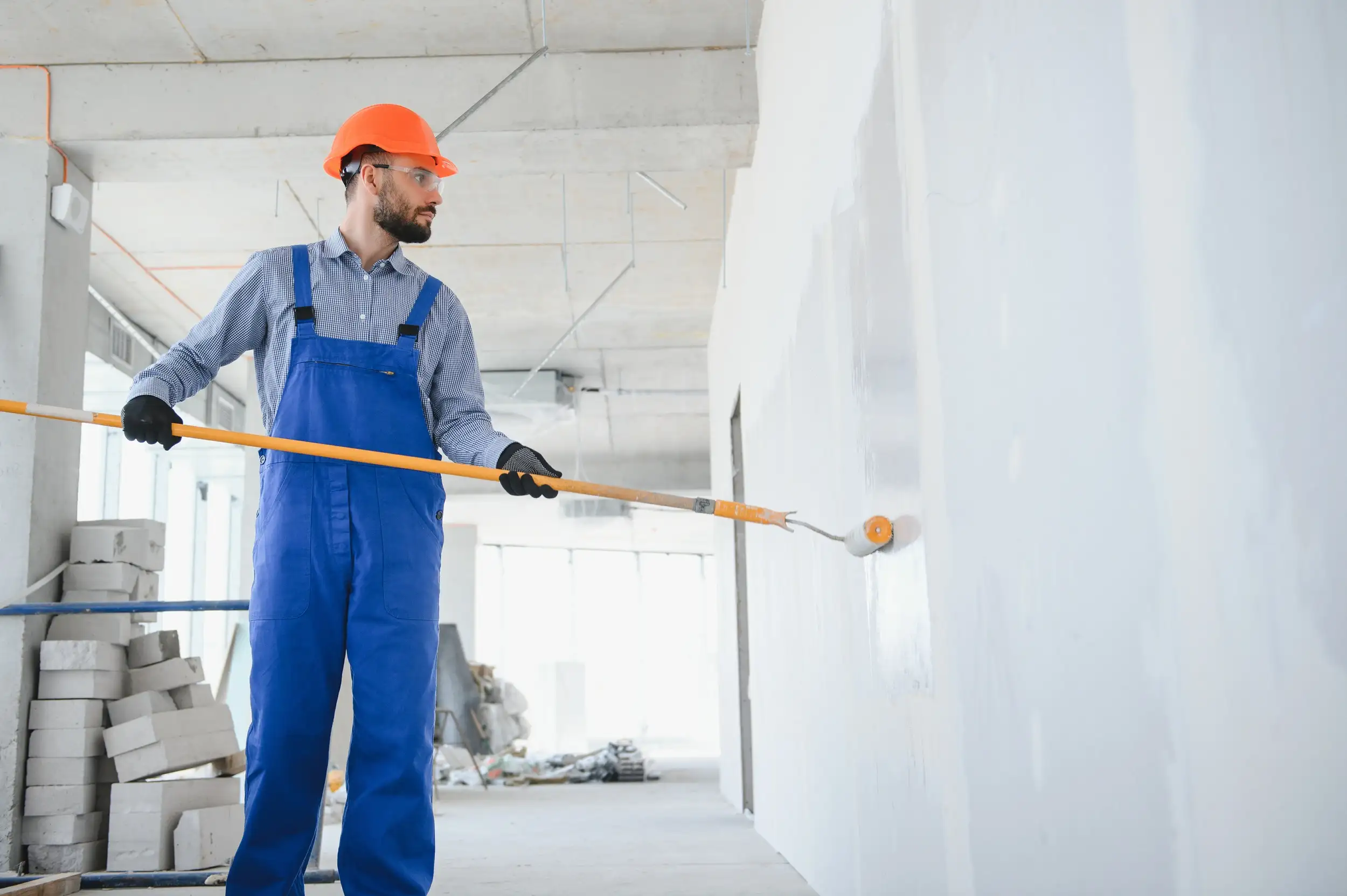 A worker painting the wall of the house with a paint roller.