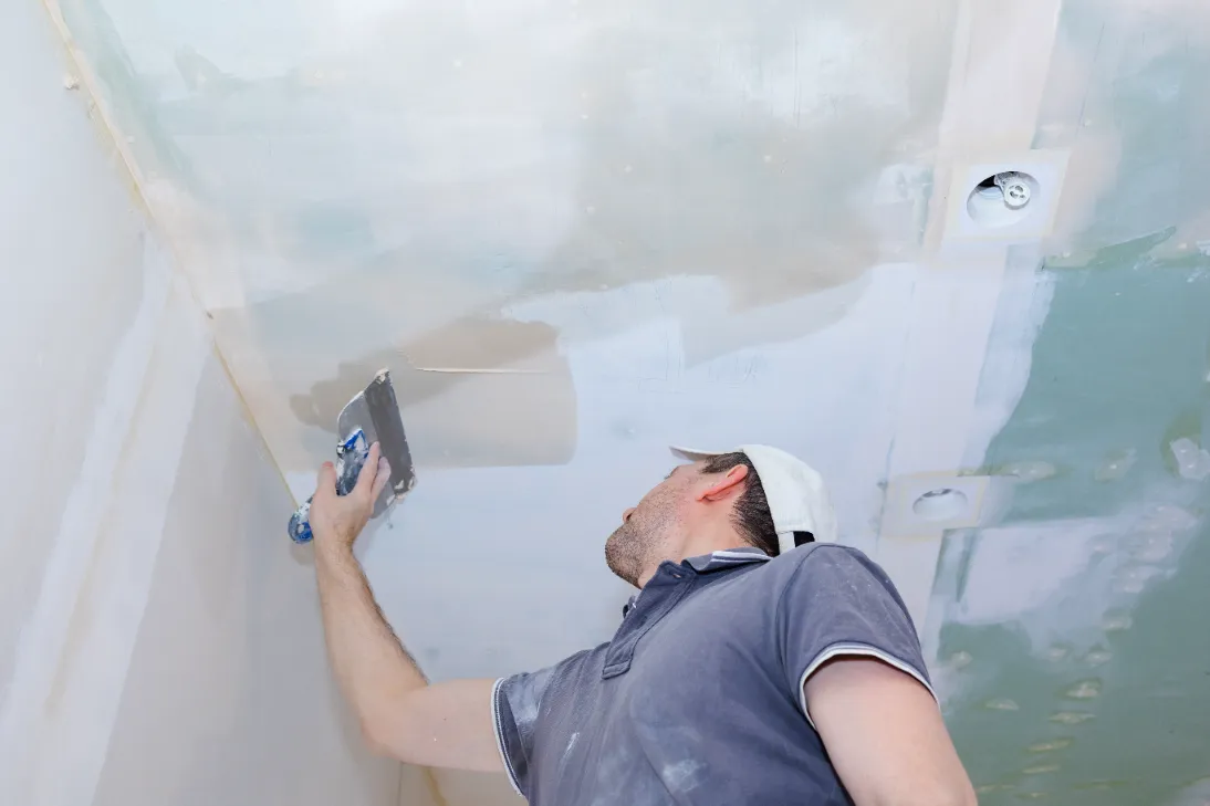 A worker repairs the new apartment ceiling with plaster.