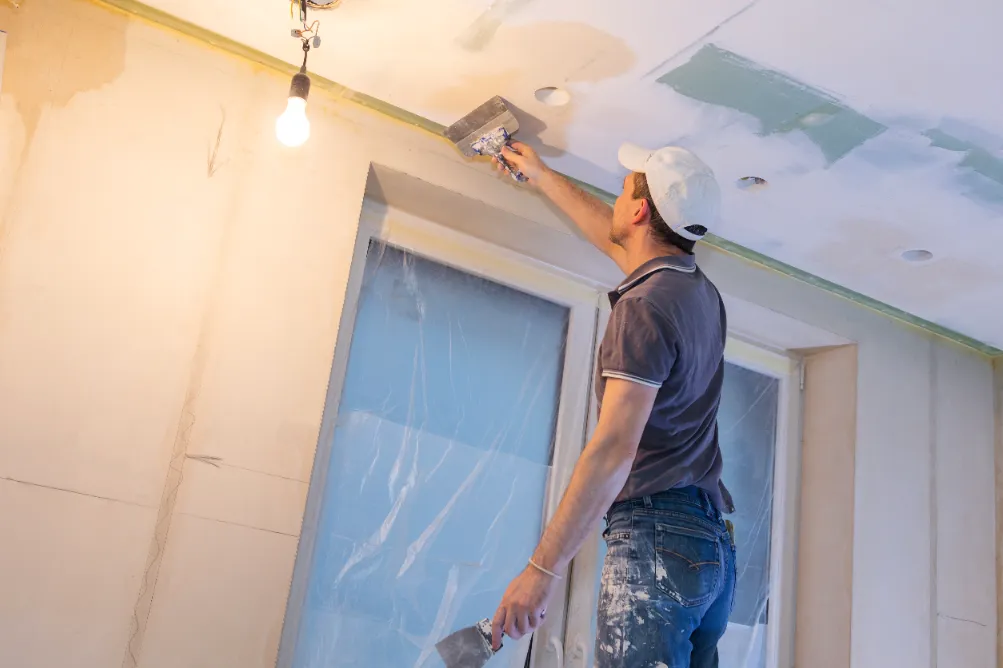 A worker servicing a drywall on the ceiling by plastering each holes.